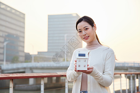 绿色节能手拿太阳能房屋模型的青年女性背景