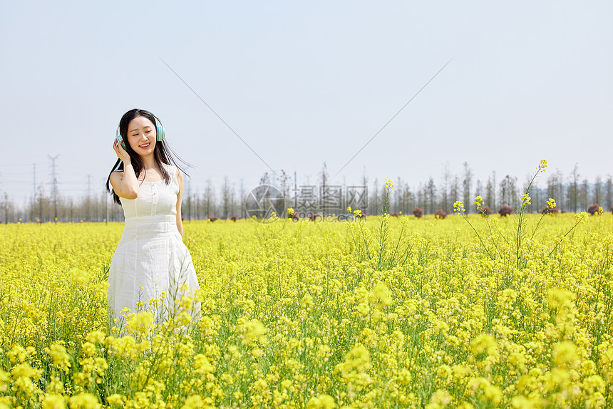 女性在油菜花海戴着耳机听歌图片