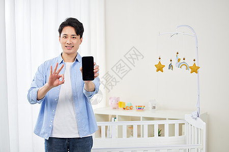 年轻奶爸布置婴儿房展示手机ok手势背景图片