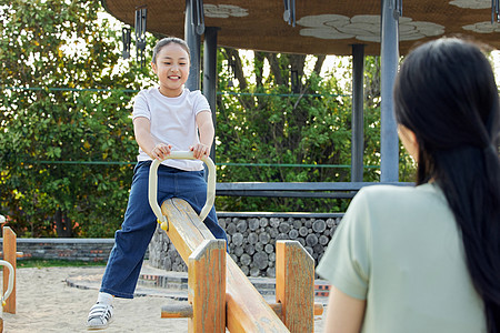 儿童节玩跷跷板母女二人在公园里玩跷跷板背景