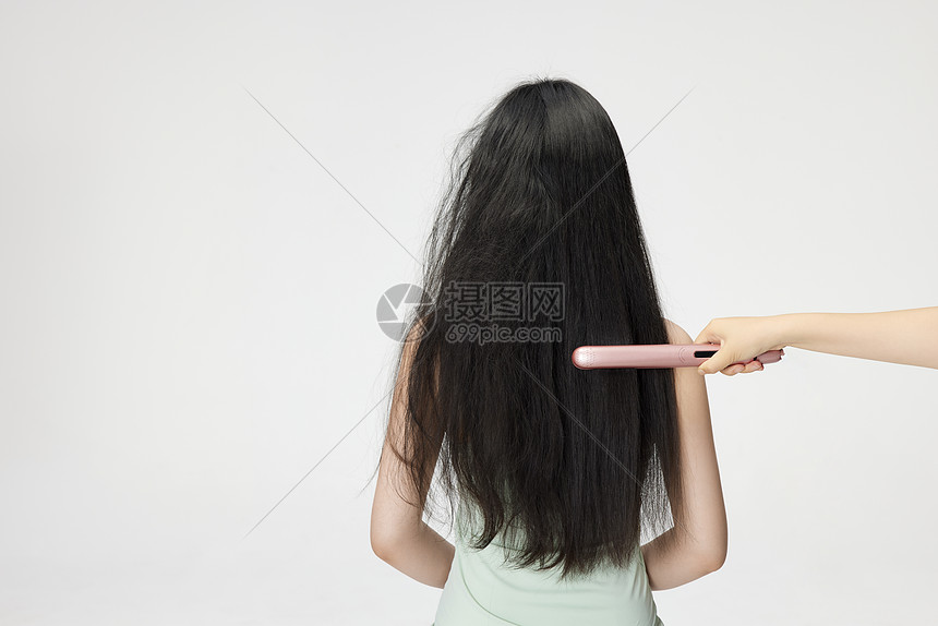 年轻女性使用夹板拉直头发背影图片