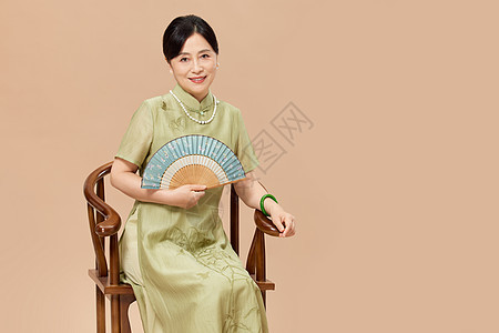 穿旗袍的中年女性手拿扇子坐在椅子上图片