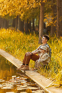 亲子游玩坐在湖边看日落的父子形象背景
