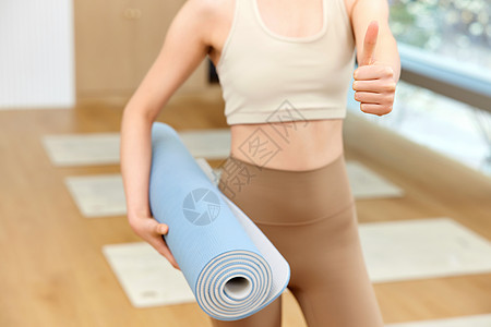 女性拿瑜伽垫竖大拇指特写图片