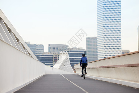城市自行车靠道路右侧骑行的男性背影背景
