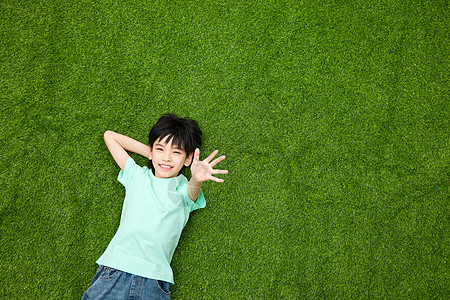 躺在草坪上开心招手的小男孩图片