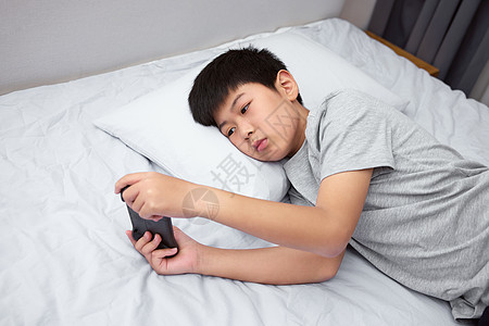 手机数据线躺在床上打游戏的男孩背景
