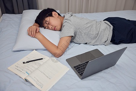 床上玩电脑男孩熬夜做作业趴在床上睡觉背景