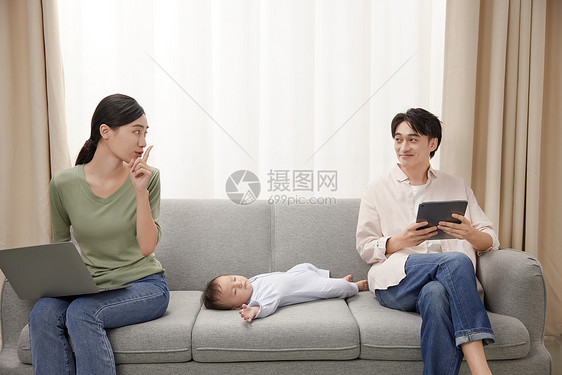 沙发上忙碌的父母担心吵醒睡觉的宝宝图片