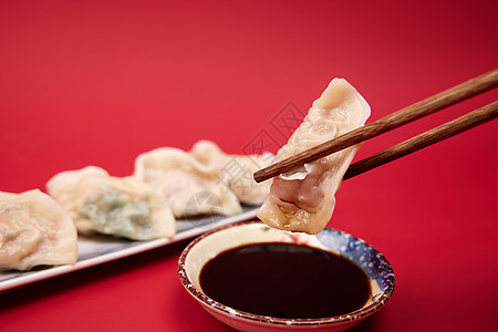 红色背景筷子夹起水饺蘸醋特写图片
