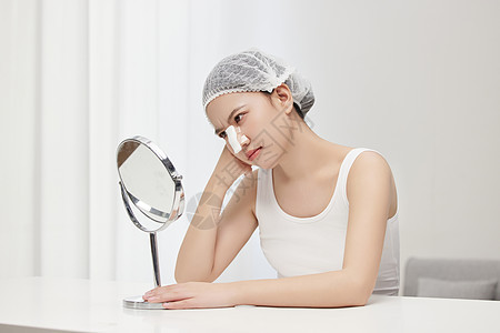镜子前皱眉思考皮肤问题的年轻女孩图片