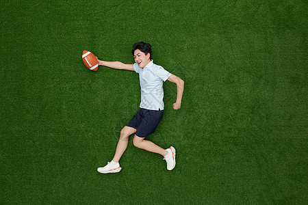 创意俯拍手上拿着橄榄球的热血青年图片