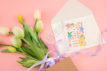 粉色桌面上一束白色郁金香和一个打开的信封图片