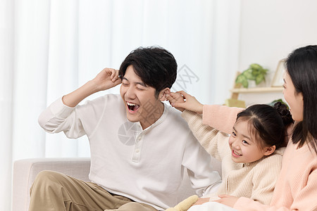 父亲教育女儿沙发上母女俩正欢快地扯着爸爸的耳朵背景