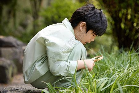 小男孩在植物园拿着放大镜观察植物图片