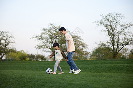 春天户外父亲和儿子在户外草地上踢足球背景