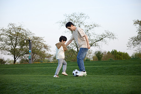 父亲和儿子在户外草地上踢足球高清图片