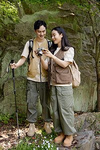 带相机的情侣漂亮女孩给男朋友看相机里拍的山上景色背景