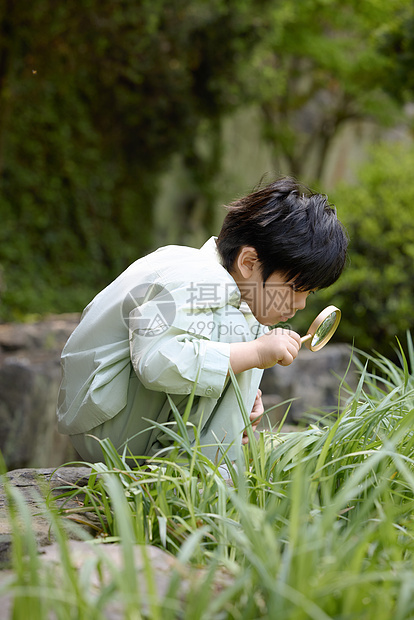 小男孩拿着放大镜蹲在地上观察植物图片