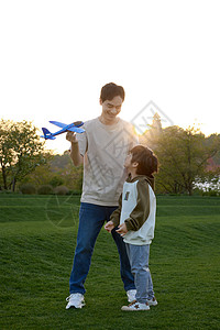 草坪上教儿子玩飞机模型的爸爸图片