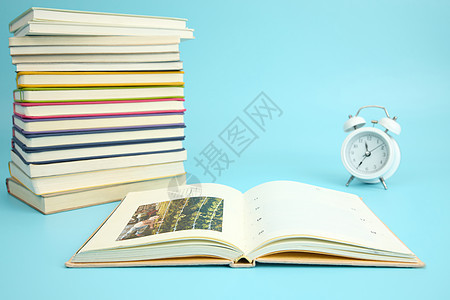 一叠彩色的书籍边有一本翻开的书与闹钟图片