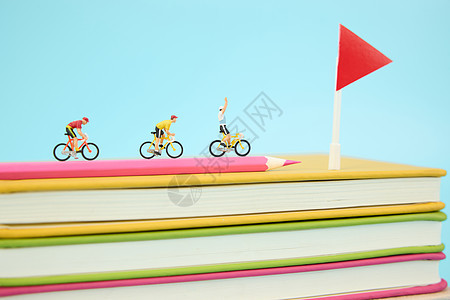 在一叠彩色书本上骑行冲向终点的微距小人图片