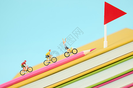 在一叠彩色书本上骑行冲向终点的微距小人图片