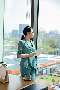 女白领拿着文件夹在落地窗前站立图片