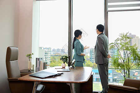 一个男白领和一位女白领站在办公室窗边讨论业务图片