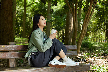 拿着咖啡杯坐在公园长椅上的美女图片