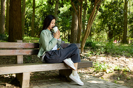 坐在公园长椅上喝咖啡的女孩图片