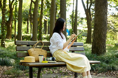 坐在森林长椅上画画的女孩图片