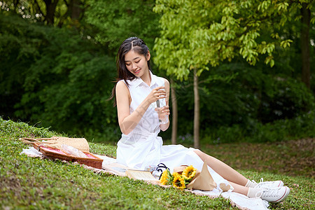 在野餐垫上喝水休息的美女形象图片