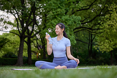 美女坐在瑜伽垫上喝水休息图片