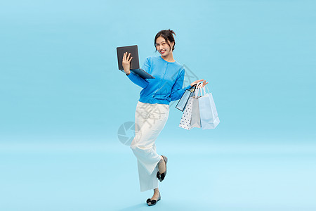 一边购物一边抱着电脑开心办公的美女图片