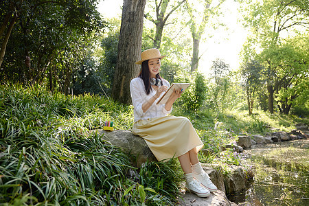 户外坐在石头上写生的美女图片