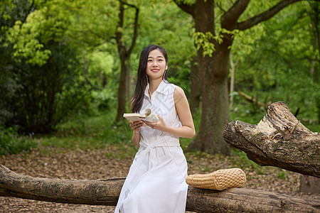 坐在粗壮树干上看书的美女图片