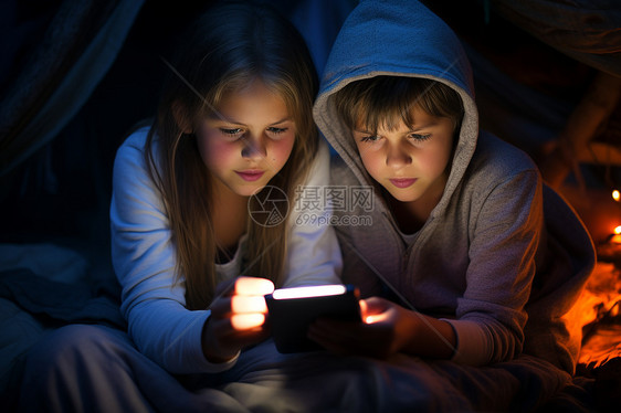 黑暗中两个孩子一起看着平板电脑图片