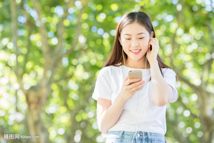 树下用手机听音乐的甜美女生