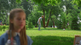 年轻的父亲在公园里休息的女儿身后传球给活跃的儿子视频素材