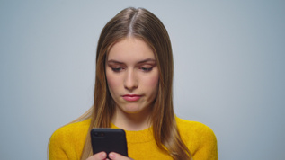 在灰色背景上使用智能手机的令人沮丧有吸引力女人肖像视频素材