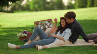 男女青年在户外欢笑坐在公园的毯子上视频素材