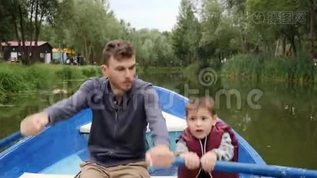 年轻的父亲和他的小儿子一起坐船在绿树丛中。 快乐的一家人周末在湖边公园玩得开心。mov格式视频下载_正版视频编号2694357-摄图网
