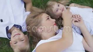 漂亮的金发女人和她的两个孩子躺在公园的草地上。 小男孩，小女孩和成年女人mp4格式视频下载_正版视频编号1867969-摄图网
