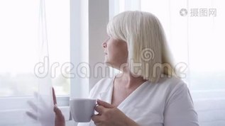 体贴成熟的女人拿着一杯茶或咖啡看着窗户。 妈妈在想她的孩子mp4格式视频下载_正版视频编号3445410-摄图网