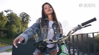 穿着时髦衣服的迷人性感女孩坐在自行车上，看着相机，夕阳下带着可爱的微笑mov格式视频下载_正版视频编号2620814-摄图网