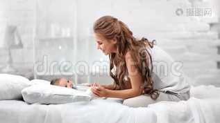微笑的母亲享受爱抚，可爱的婴儿躺在床上，周围是白色的房间内部mov格式视频下载_正版视频编号3373725-摄图网