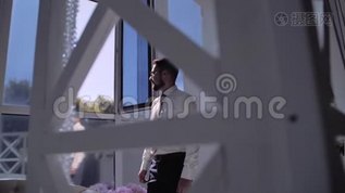 戴着眼镜和白衬衫的时髦男人站在明亮的窗户前，看着它。mp4格式视频下载_正版视频编号1800877-摄图网