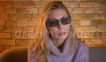 成年白种人金发女性在电视上用3D眼镜观看3D的特写镜头，带有好奇的面部表情视频下载-实拍视频-正版视频1801092-摄图网