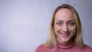白种人年轻的金发女子在灰色背景下谦卑地微笑着进入镜头的肖像。mov格式视频下载_正版视频编号3455430-摄图网